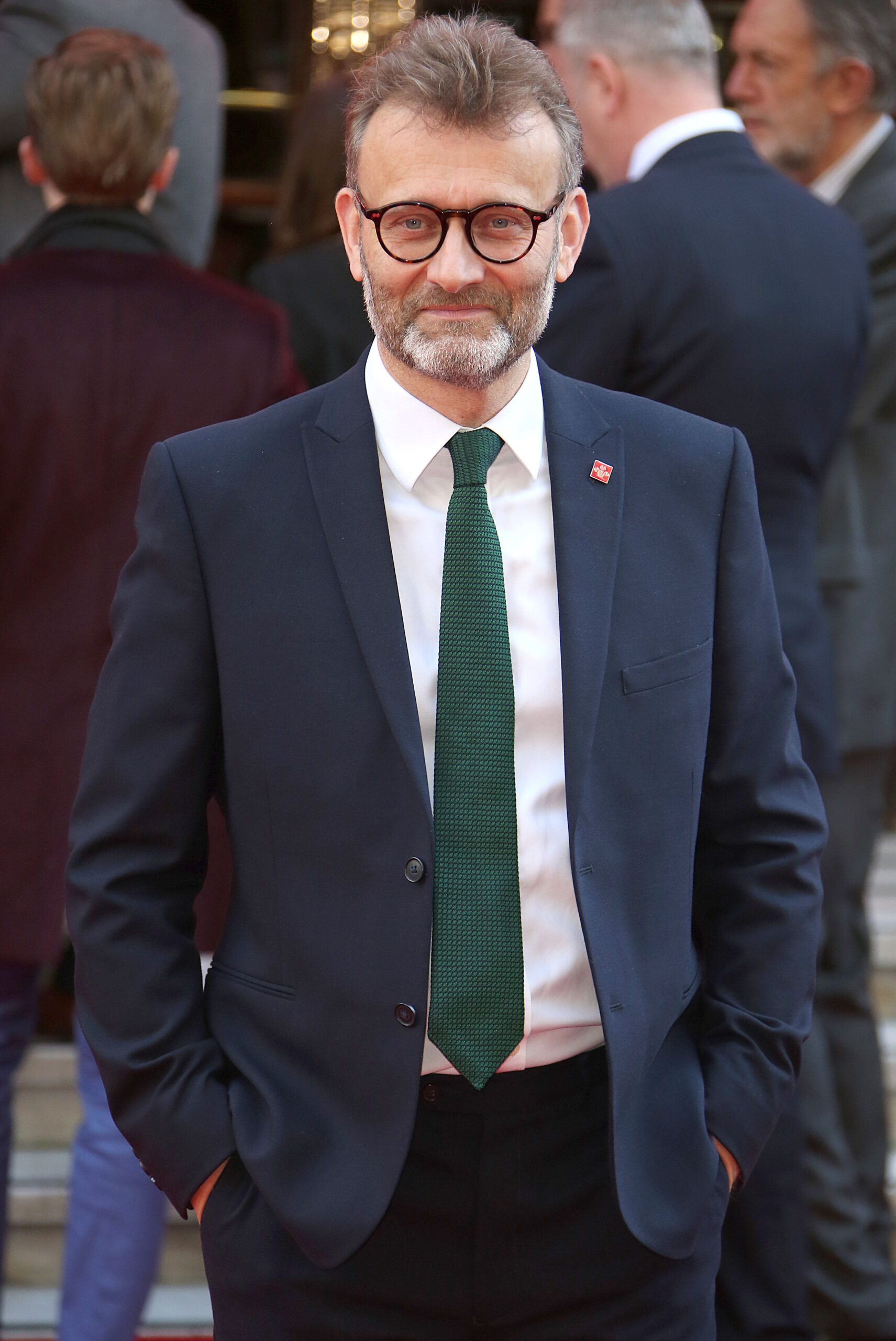 Hugh Dennis wears a navy suit and smiles at the camera