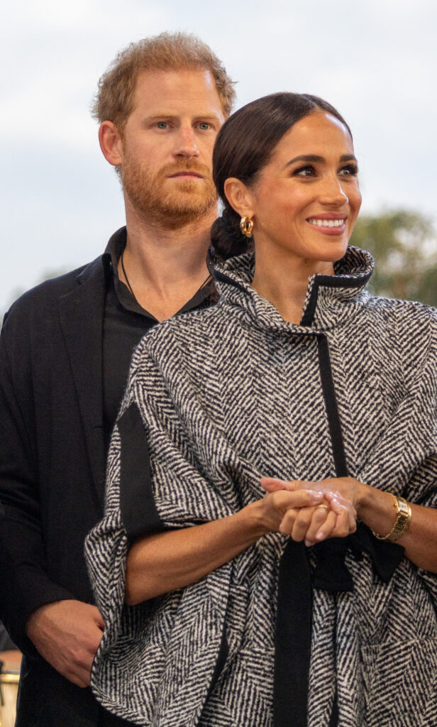 Prince Harry looks serious as he stands behind smiling Meghan Markle at Invictus Games