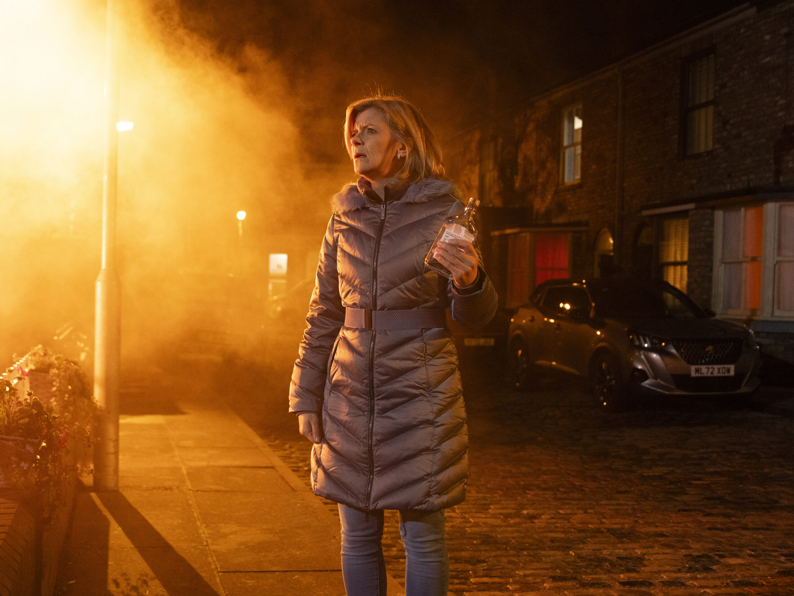 Leanne with bottle of vodka, standing outside of fire