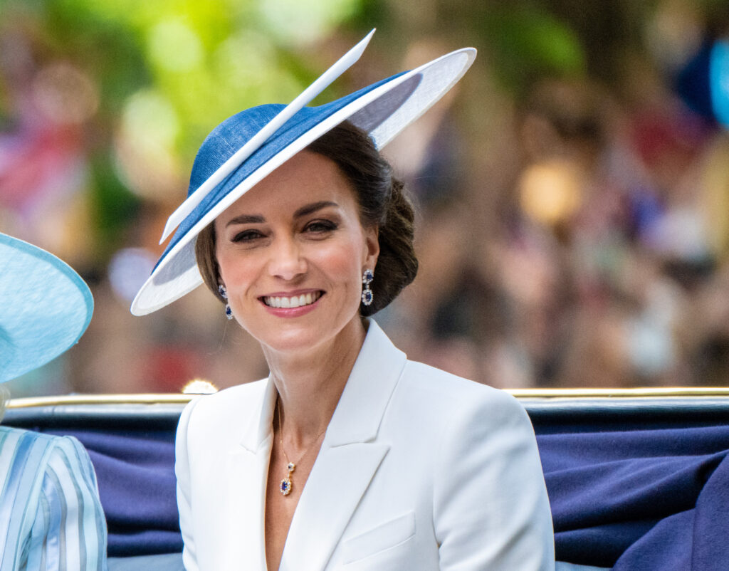 Princess Kate sitting in a carriage in a white suit and matching hat
