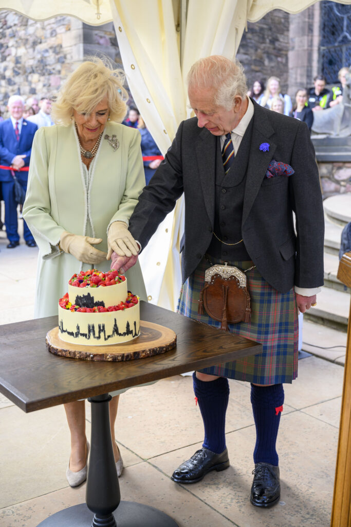 Queen Camilla and King Charles cutting a cake during royal engagement