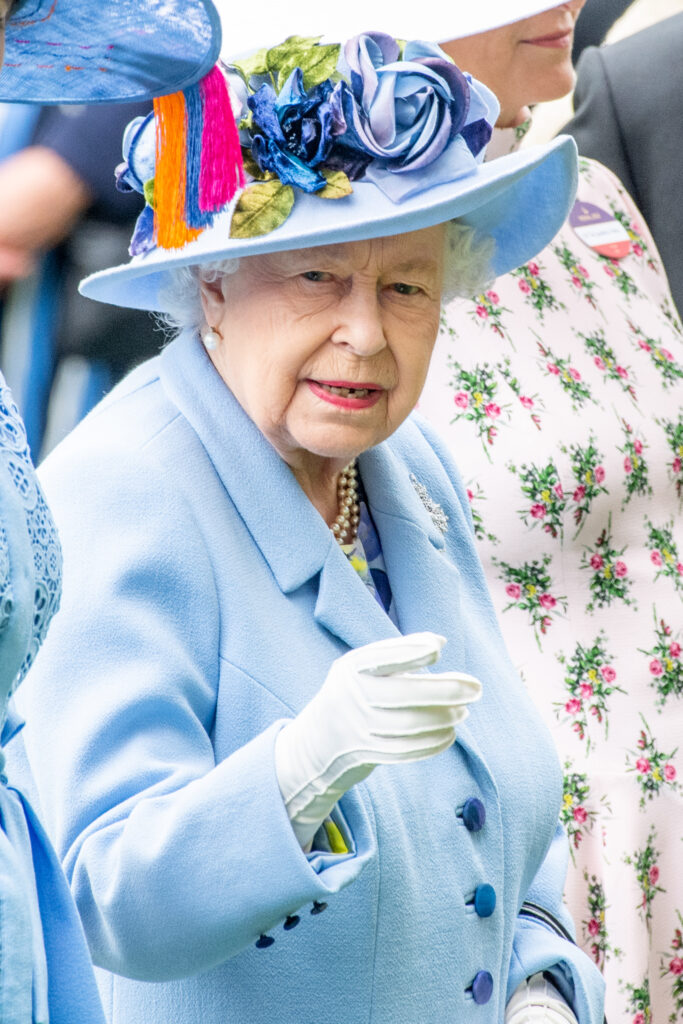 Queen Elizabeth II pointing in light blue dress and hat at races