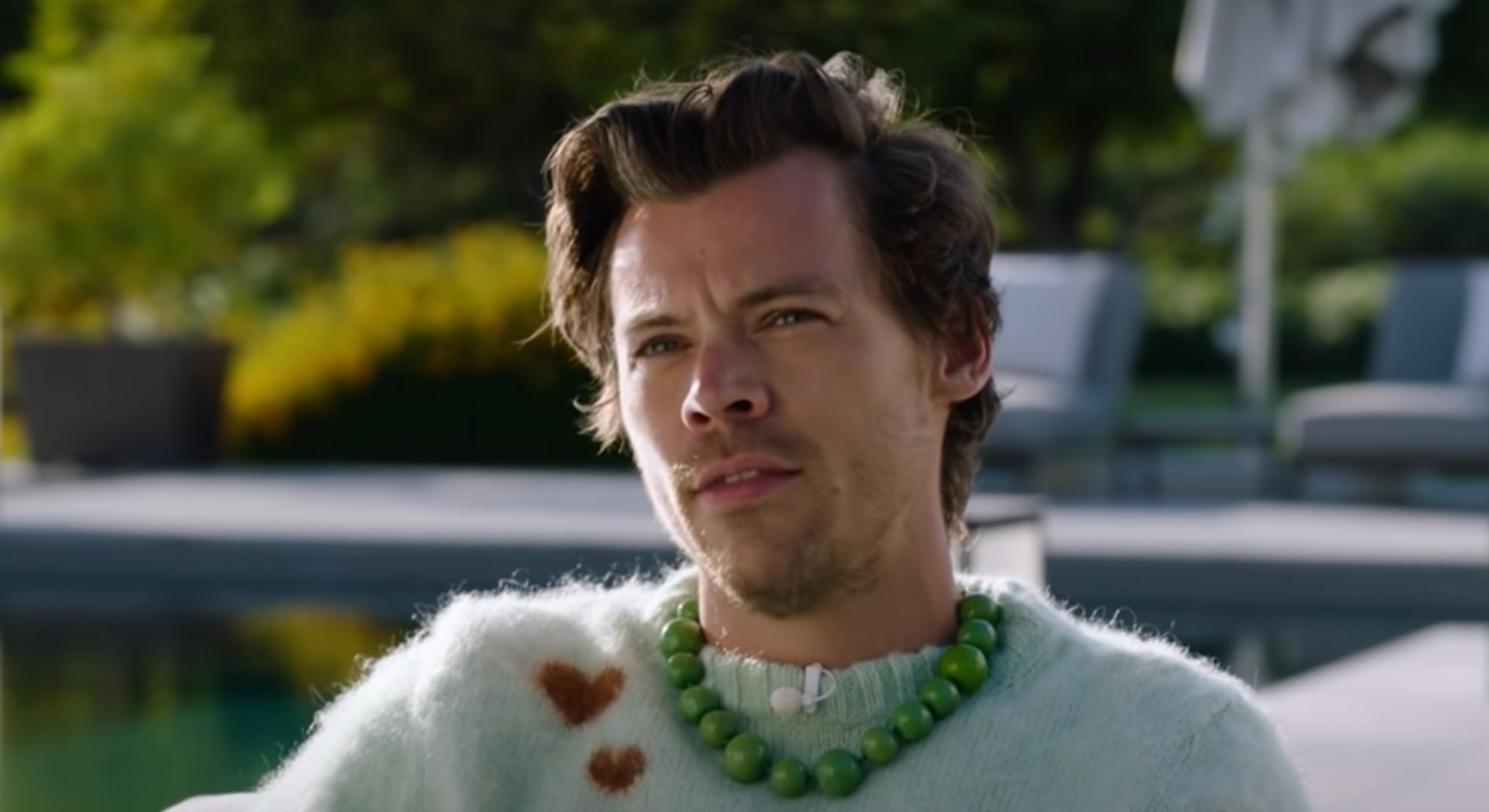Harry Styles wears a knitted jumper and sits outside in the sunshine