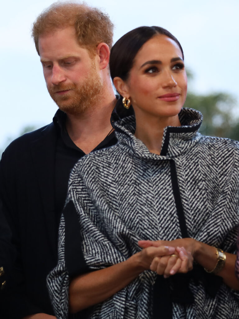 Prince Harry looks down as Meghan Markle clasps her hands