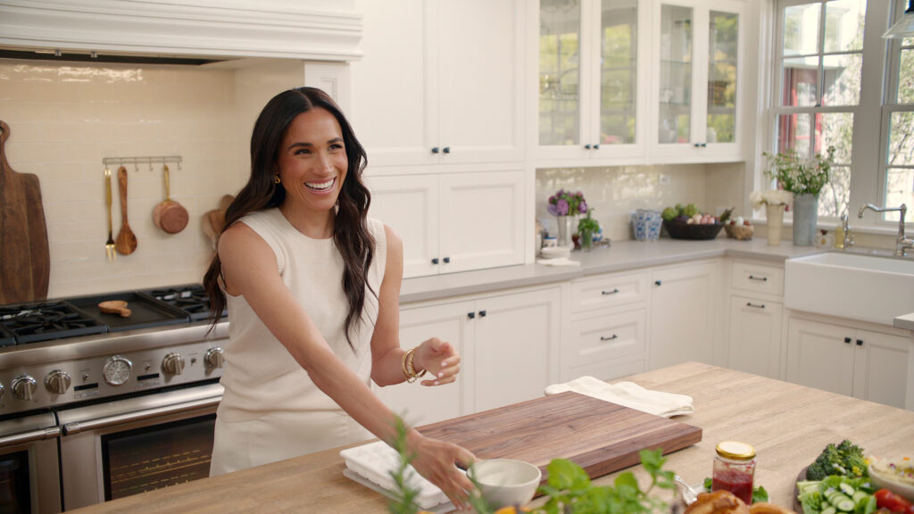 Meghan Markle smiles as she drinks a cup of coffee