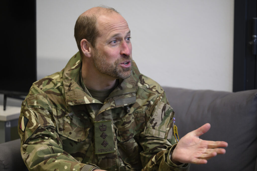 Prince William wears a military jacket and sits on a sofa
