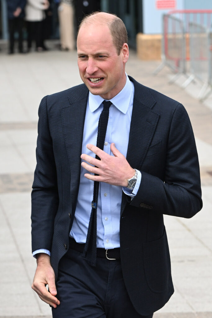 Prince William smiles as he wears a black suit and blue shirt