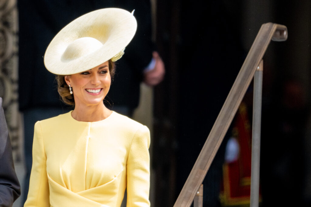 Kate Middleton wears a yellow dress and hat and smiles