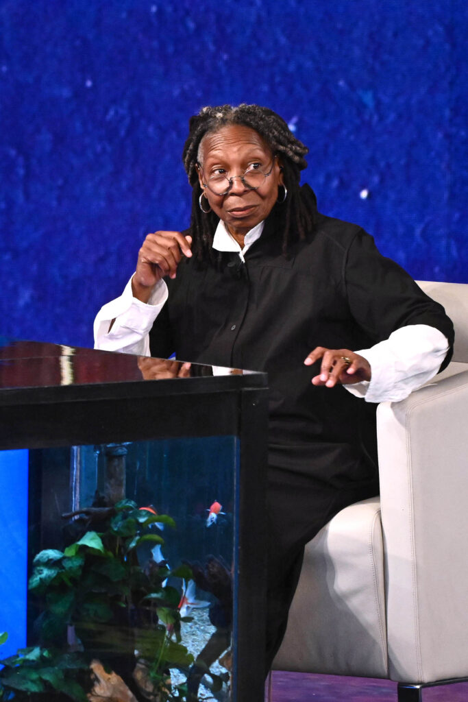 Whoopi Goldberg sits on a white chair
