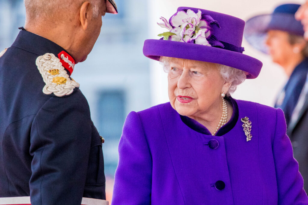 Queen Elizabeth wears a purple hat and coat
