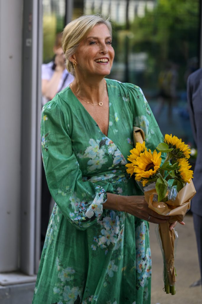 Duchess Sophie smiling wearing a green floral dress and holding sunflowers 