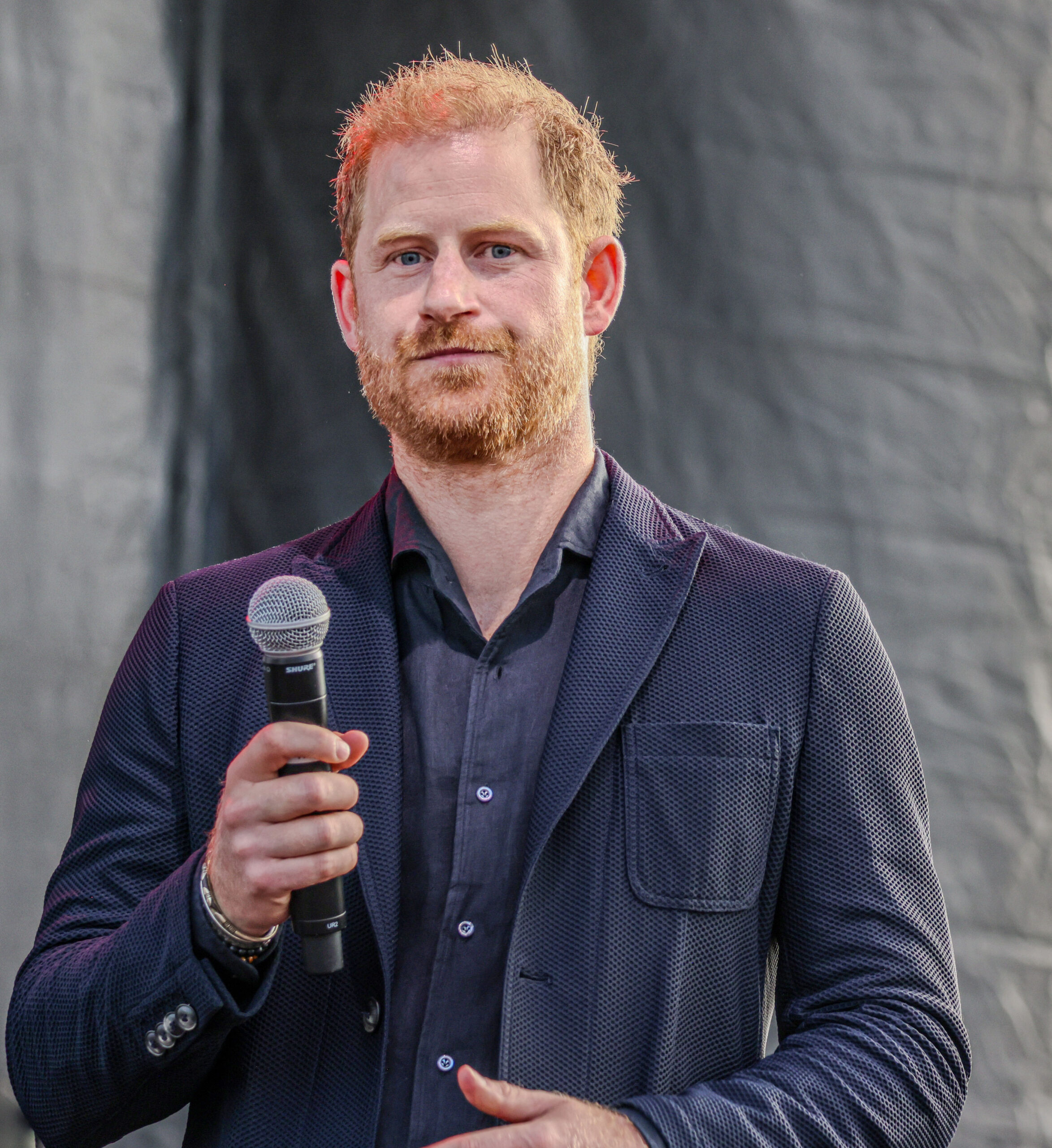 Prince Harry frowning holding a microphone