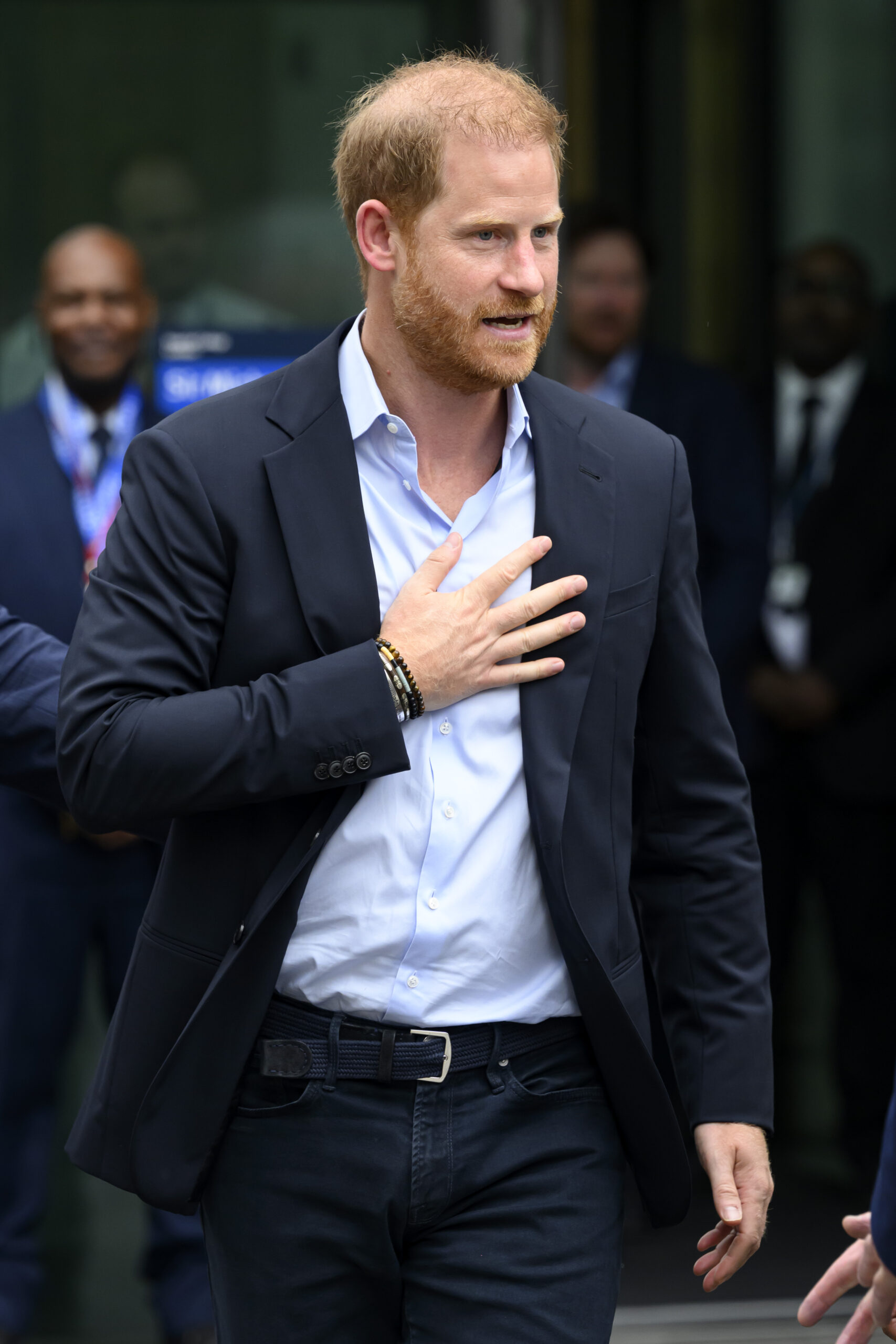 Prince Harry smiling whilst touching his stomach on UK visit