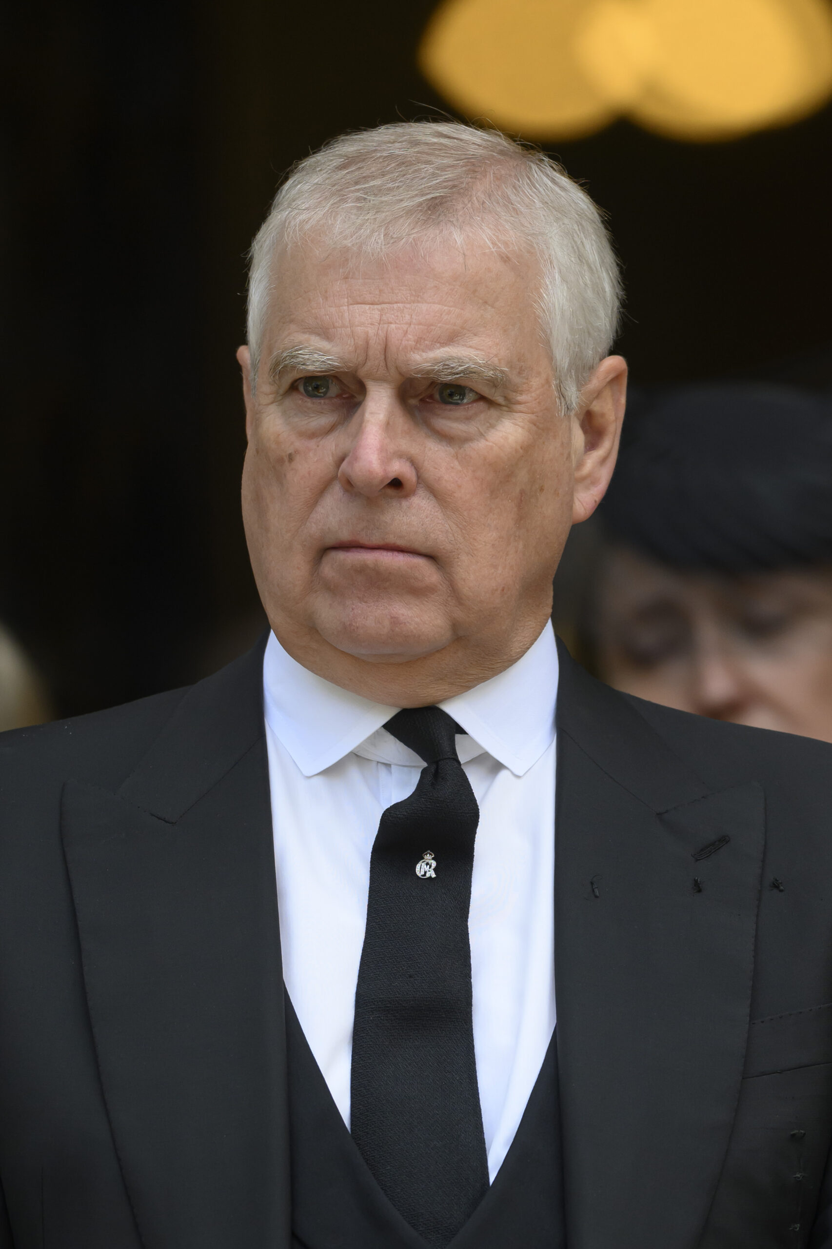Andrew Mountbatten-Windsor frowning wearing a black suit and tie