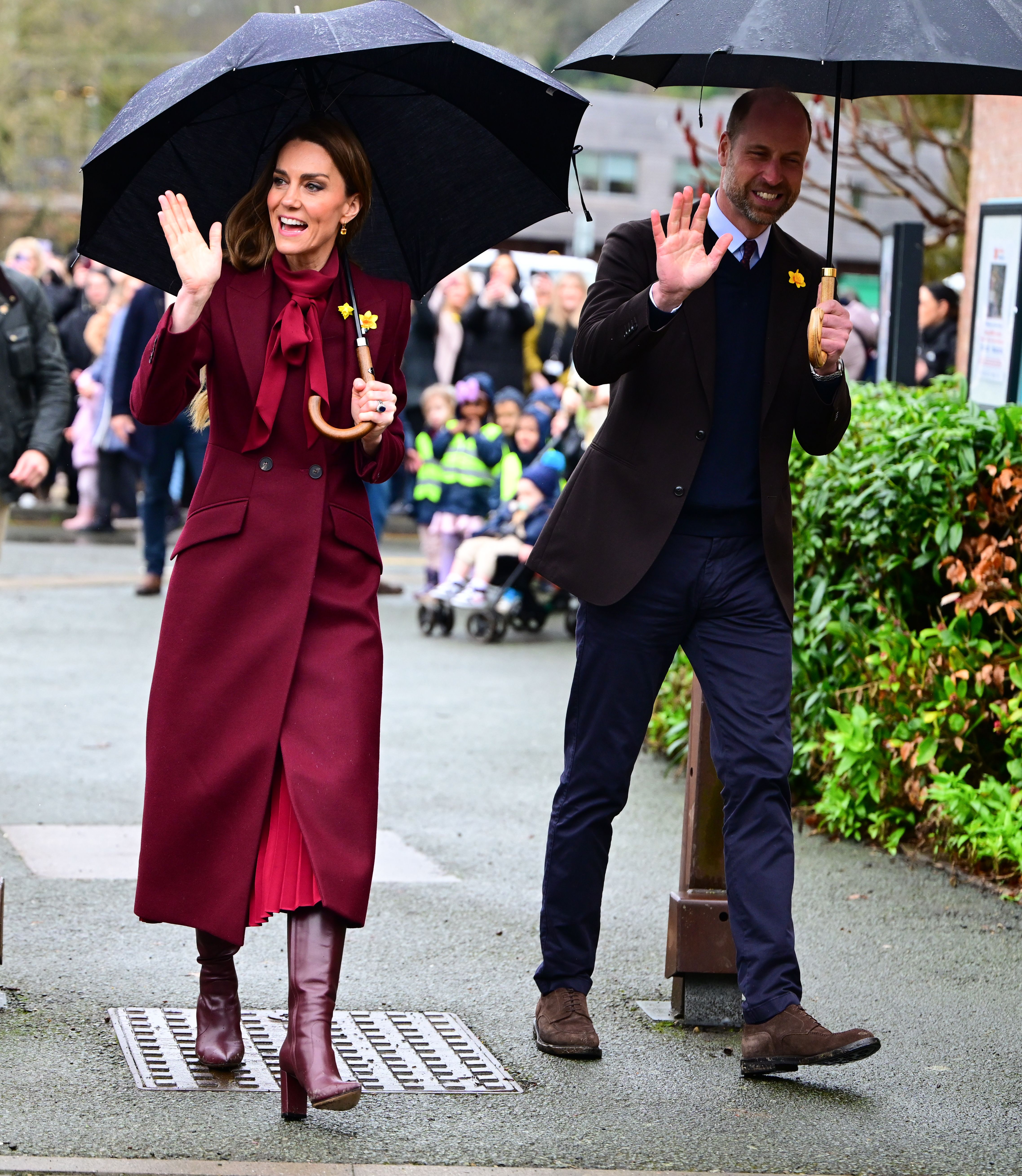 Princess Kate and prince William smiling and waving whilst holding umbrellas