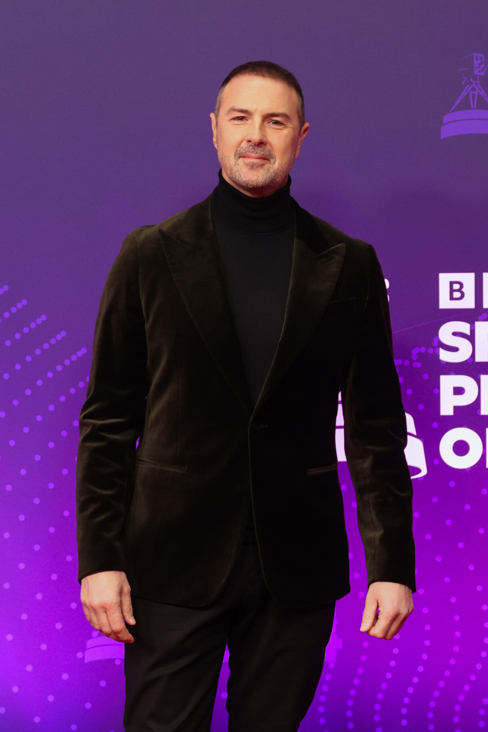 Paddy McGuinness in a black suit against a purple backdrop