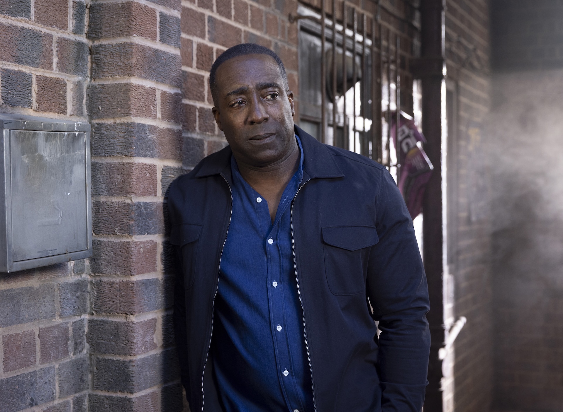 Ronnie serious while leaning up against a wall in Coronation Street