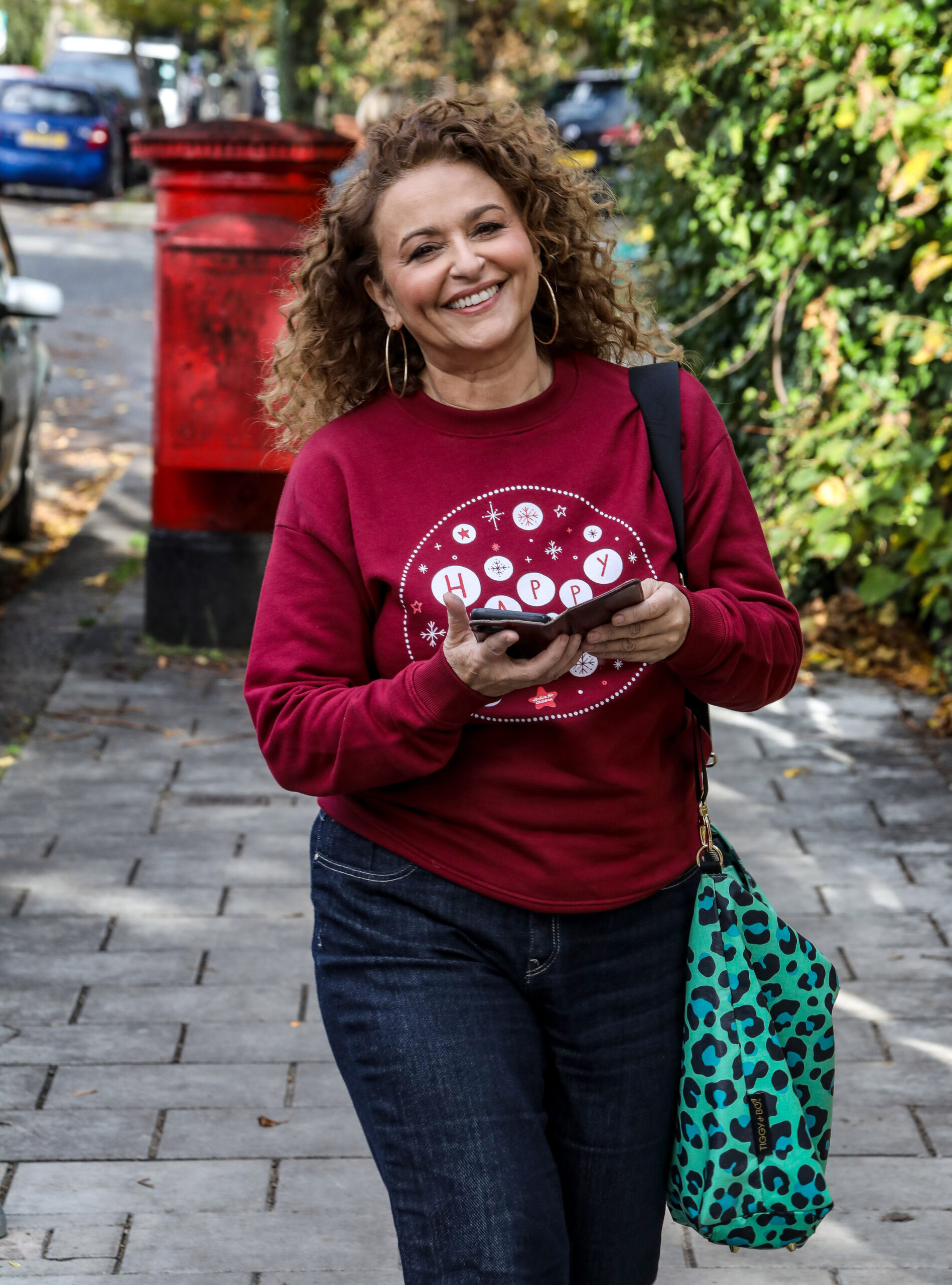 Nadia Sawalha smiling and looking up at the camera as she holds her phone