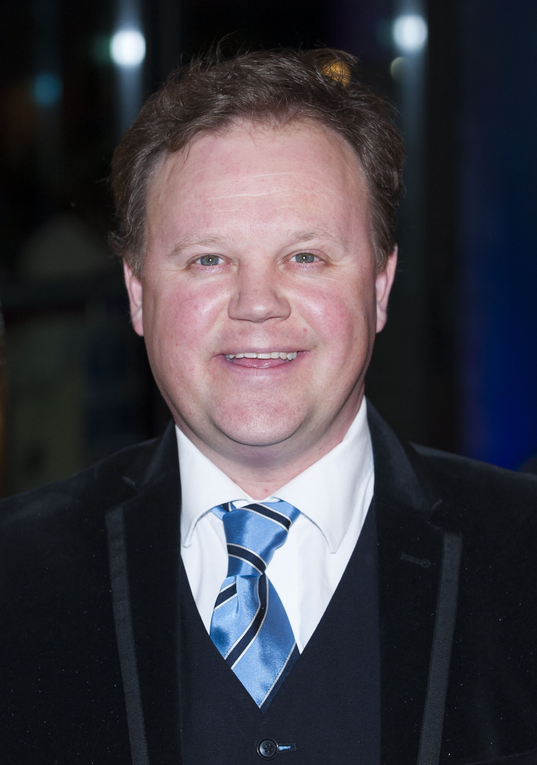 Justin Fletcher smiling wearing a suit and blue tie