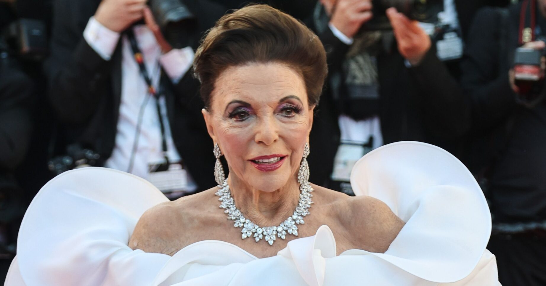 Joan Collins smiling wearing a white dress