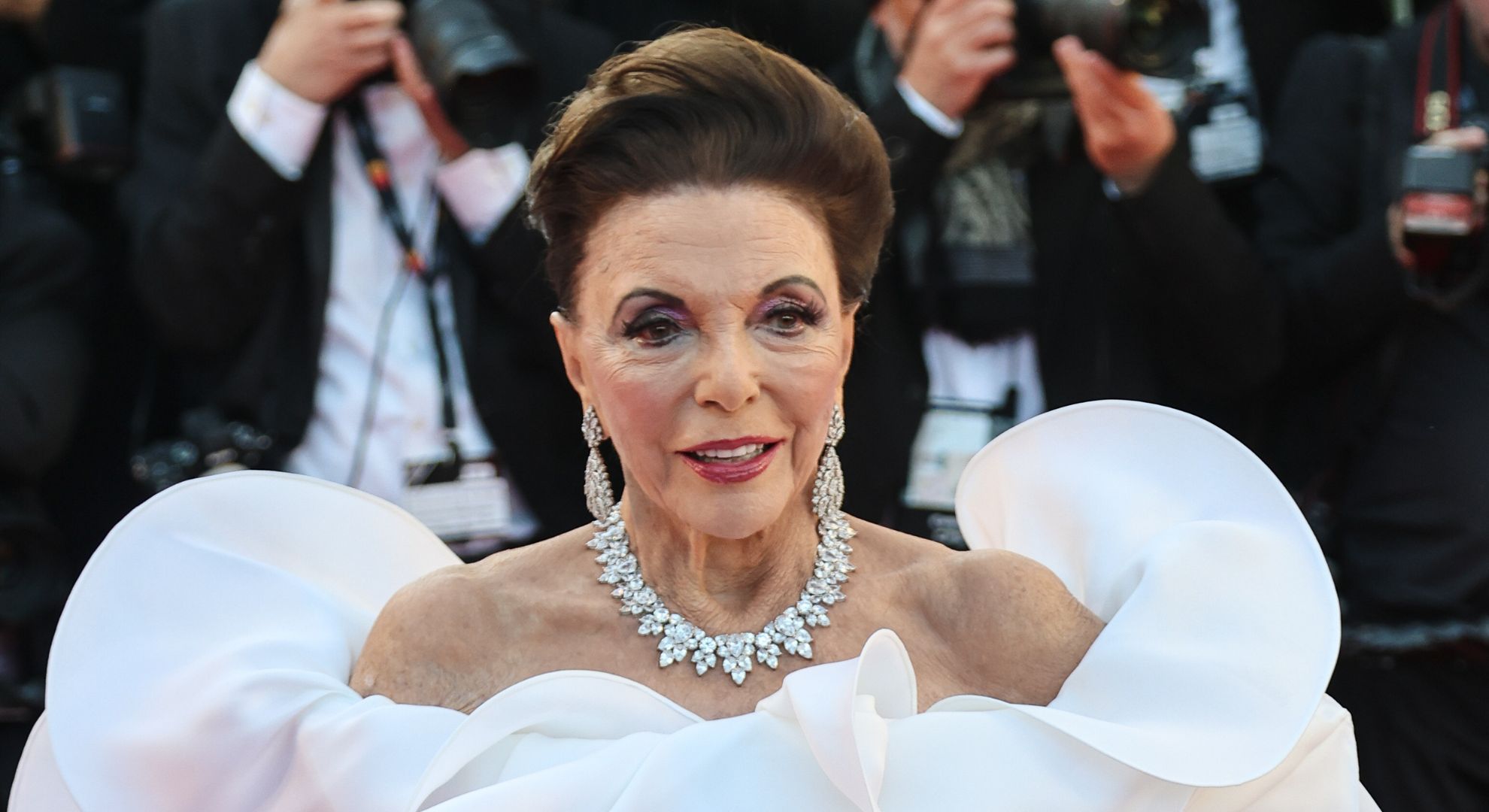 Joan Collins smiling wearing a white dress