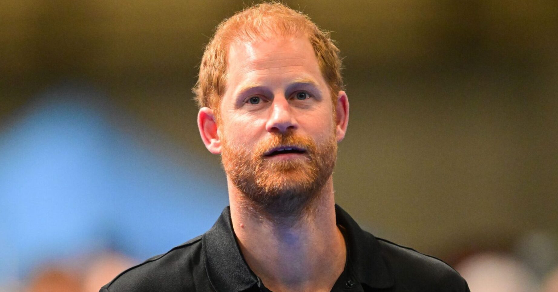 Prince Harry with a serious expression wearing an Invictus Games polo shirt