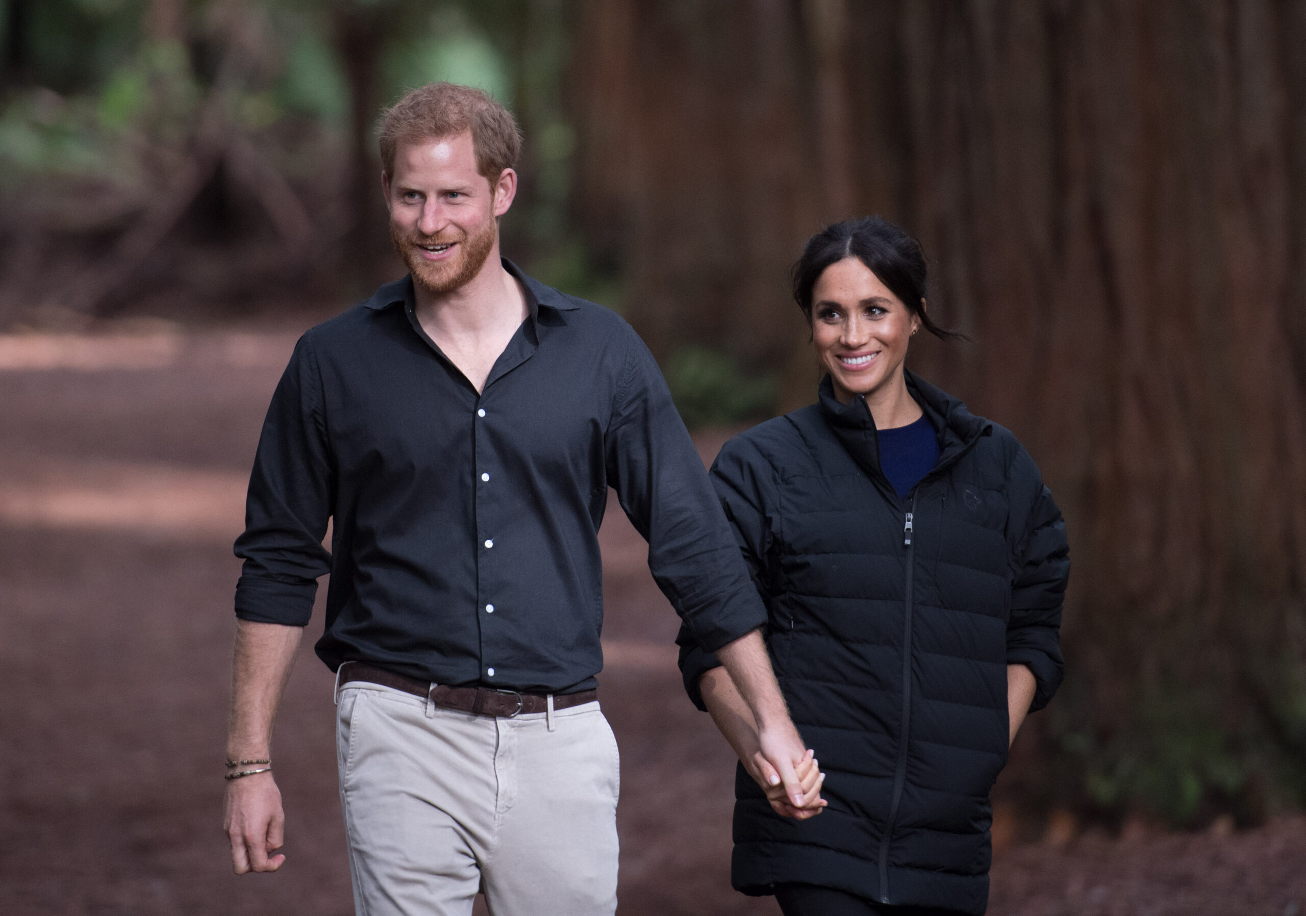 Prince Harry and Meghan hold hands as they walk through the woods