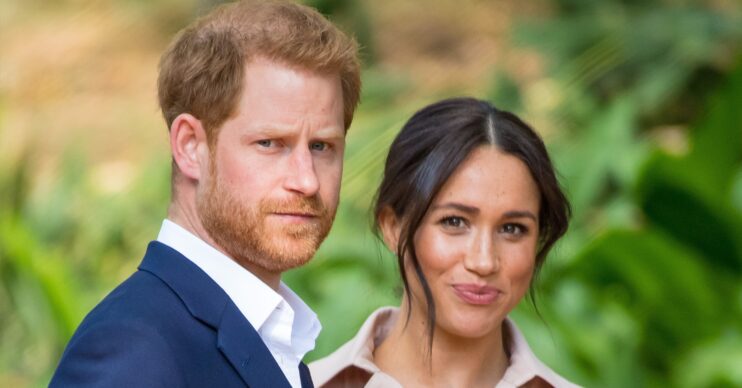 Prince Harry looking serious as Meghan Markle smiles at camera