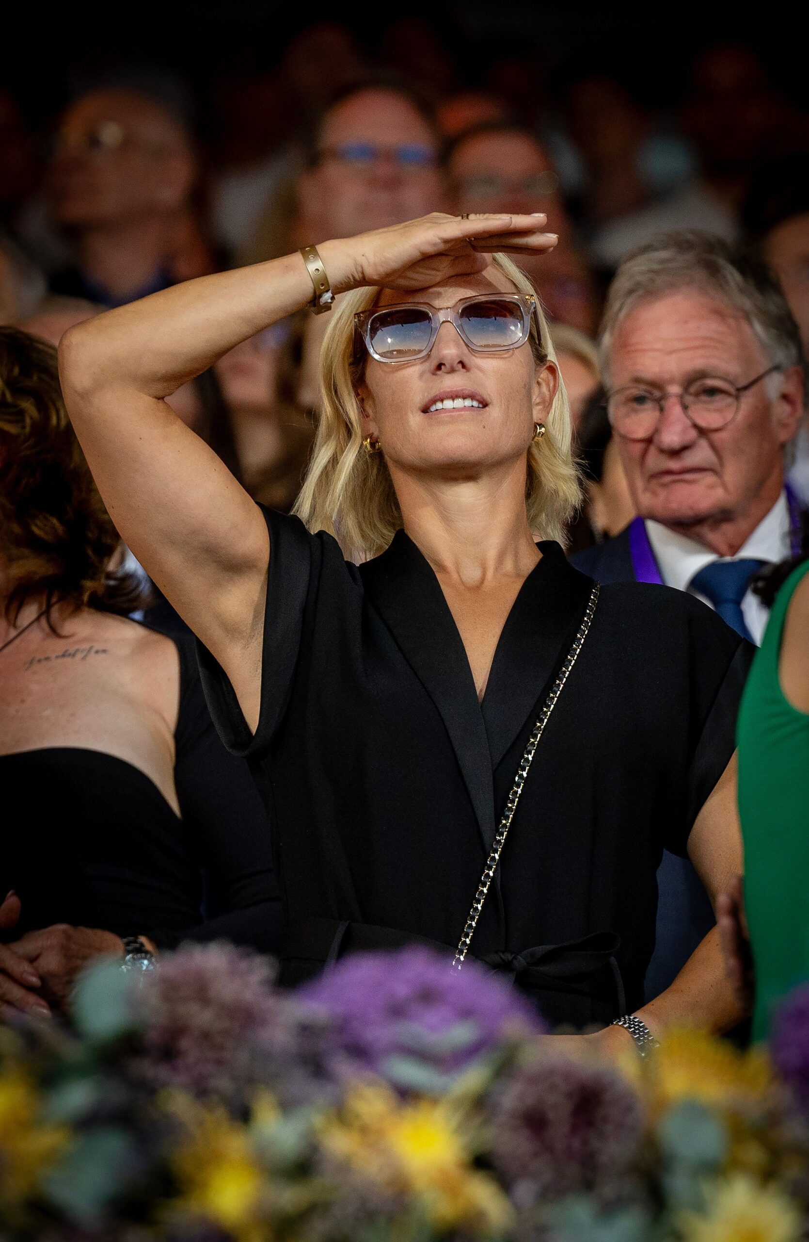 Zara Tindall wearing a black jumpsuit an sunglasses, shielding her face from the sun