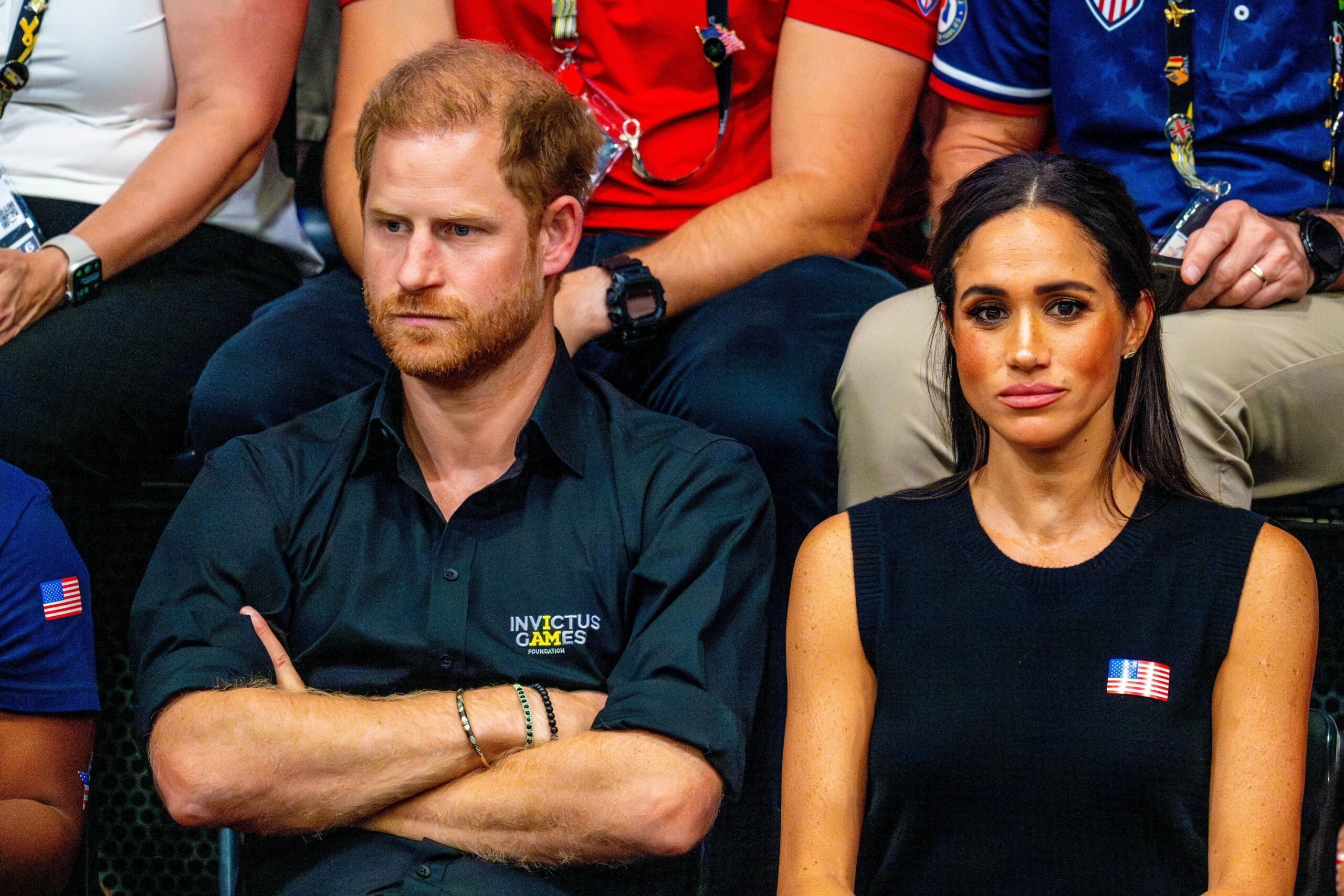 Prince Harry folds his arms while Meghan looks bored