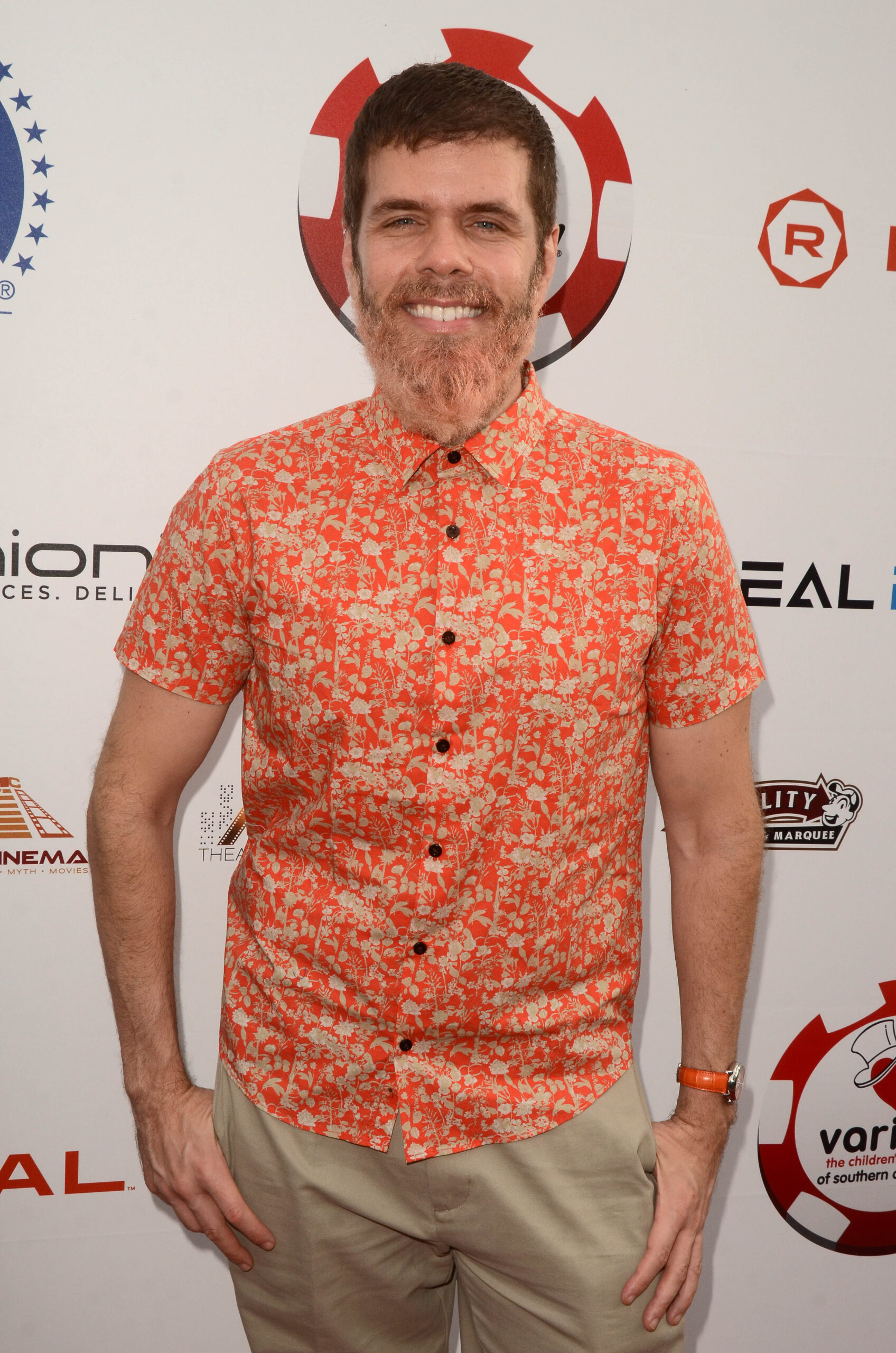 Perez Hilton wears a orange shirt and has a beard