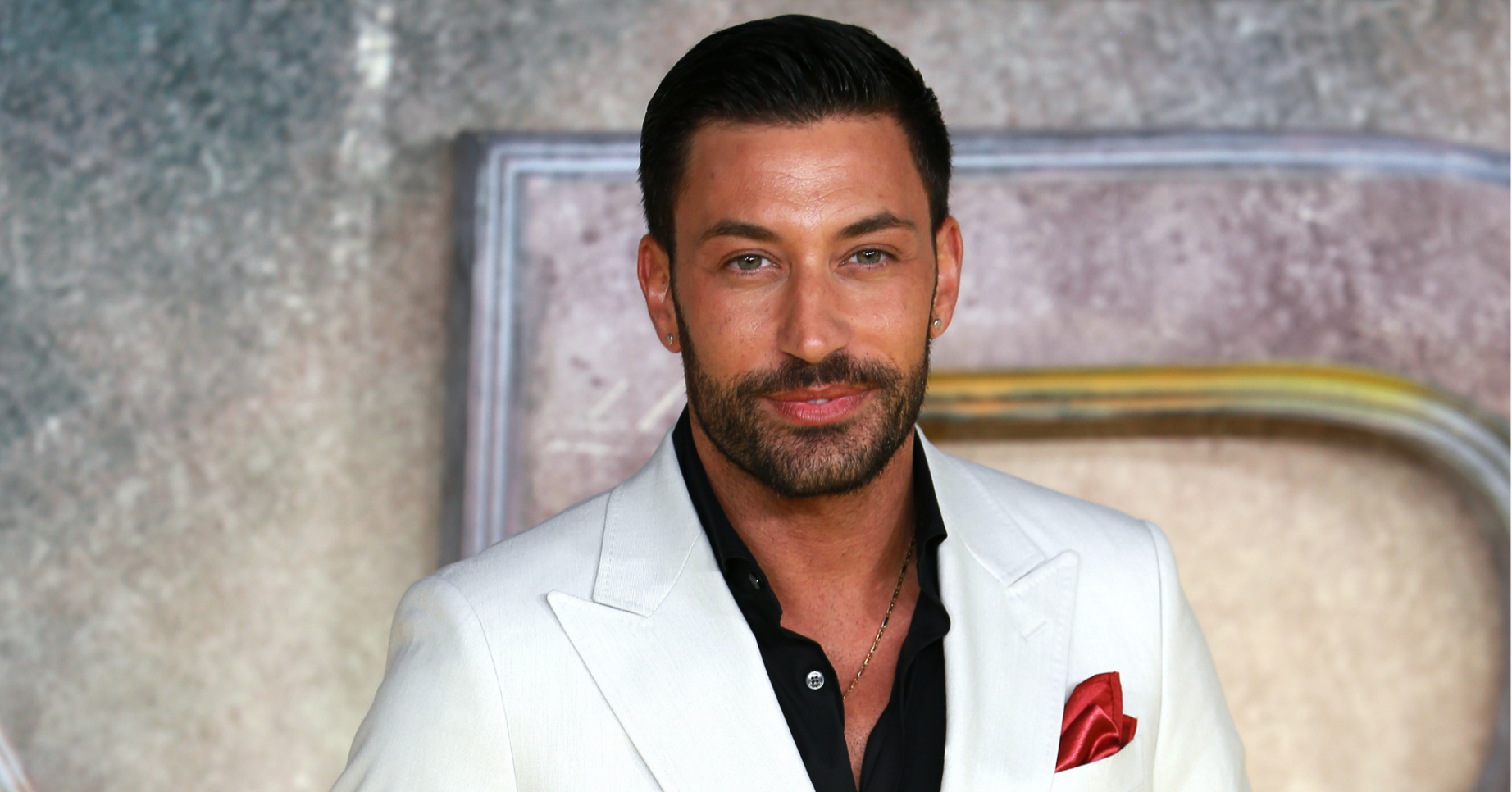 Giovanni Pernice wears a white suit on the red carpet with a black shirt unbuttoned at the top