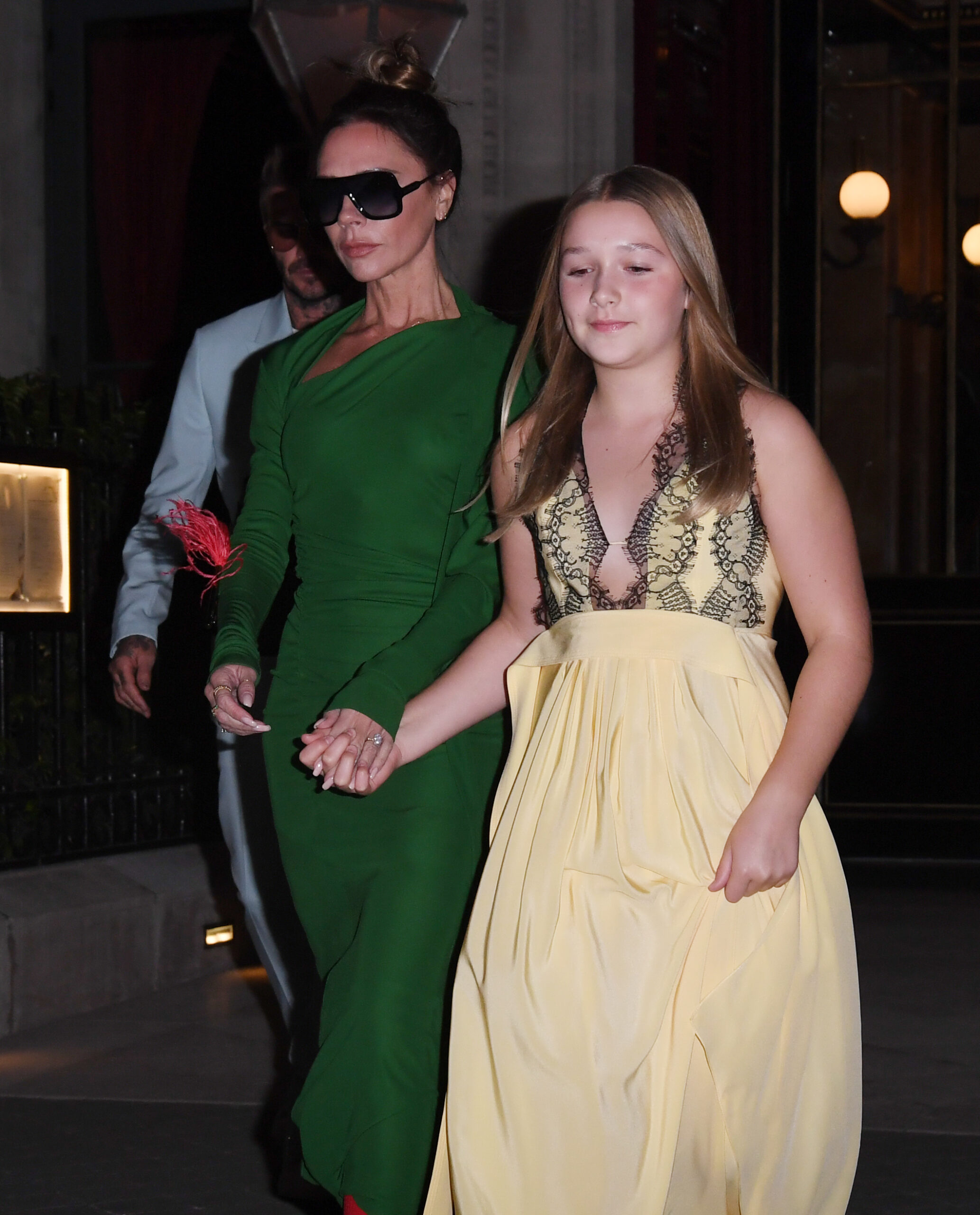 Victoria Beckham in green dress and sunglasses walking alongside Harper